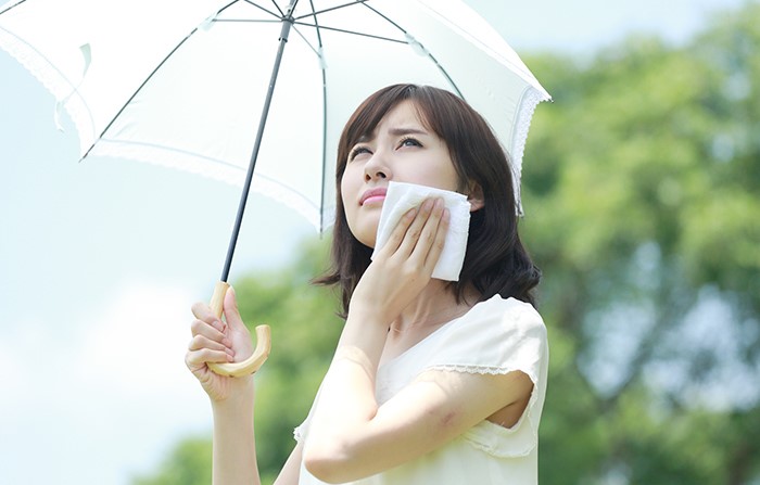 日傘をさして汗を拭う女性