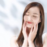 日差しを浴びながら両手で肌に触れている目を閉じた女性