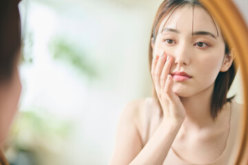 頬に手を当て、鏡を見ながら落ち込む表情をする女性